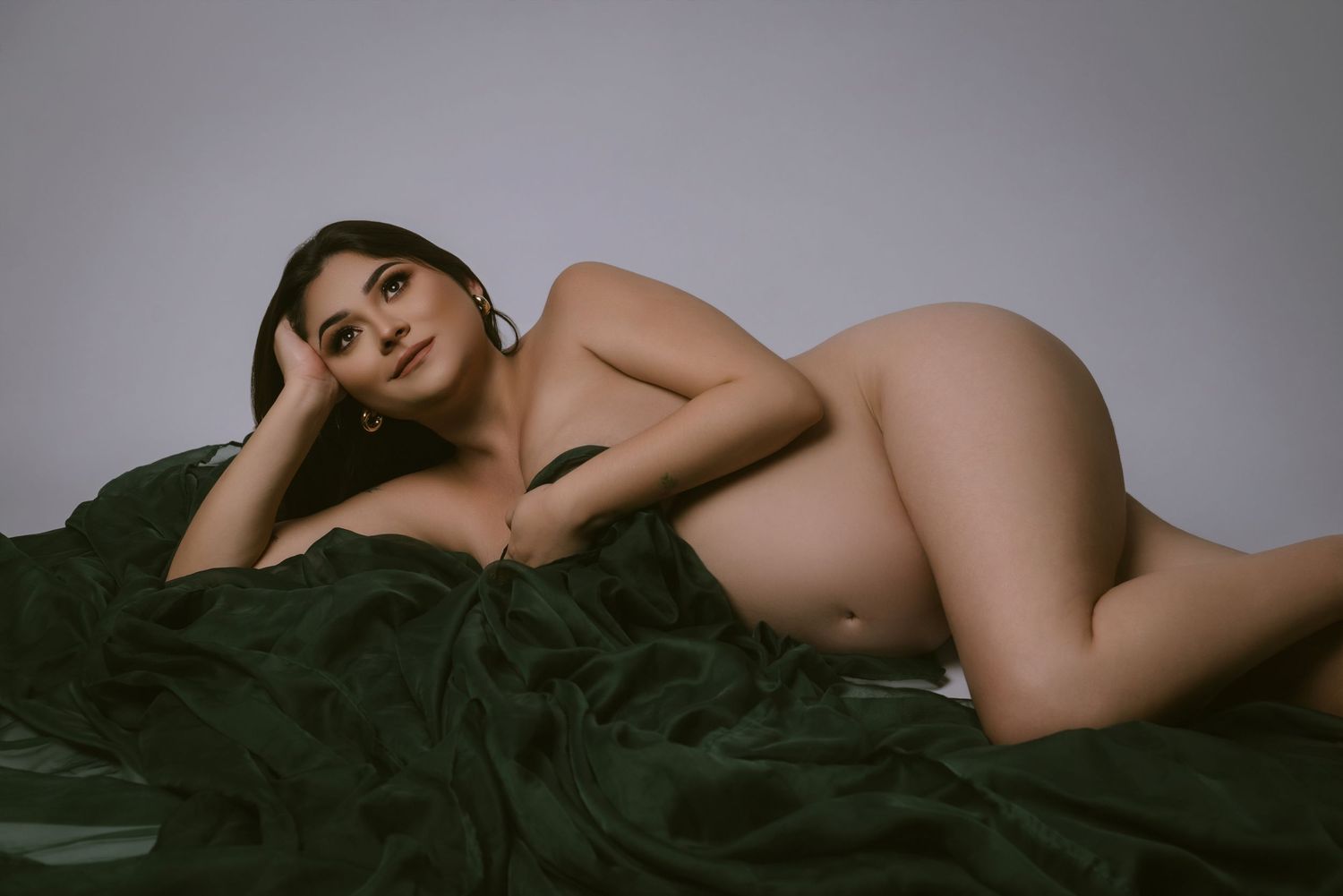 Artistic boudoir photo of figure reclining on dark fabric in dramatic lighting.