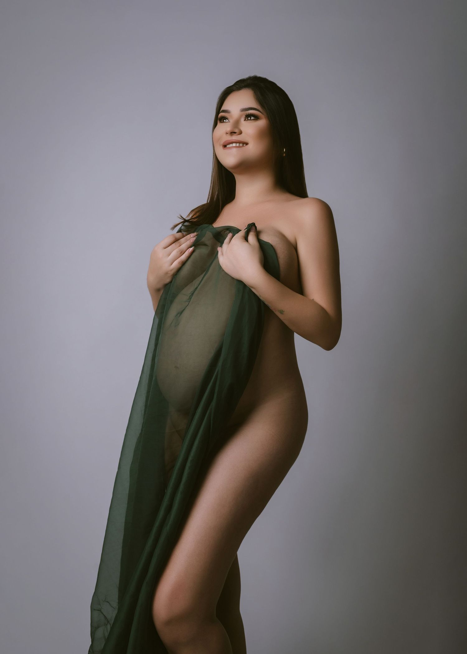 Artistic maternity portrait with flowing fabric against grey background.