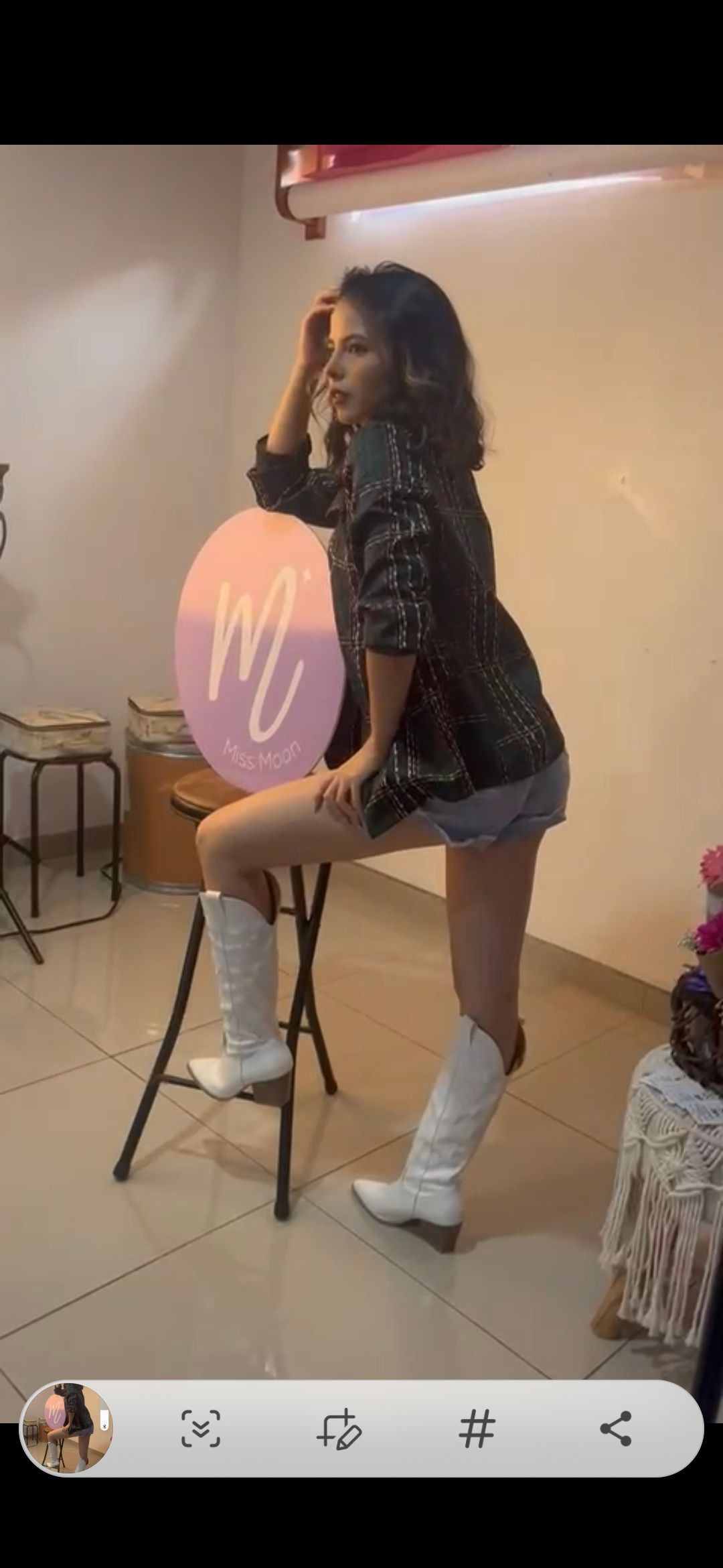 Fashion photoshoot featuring a person in white boots and dark dress posing on a stool against a light background.