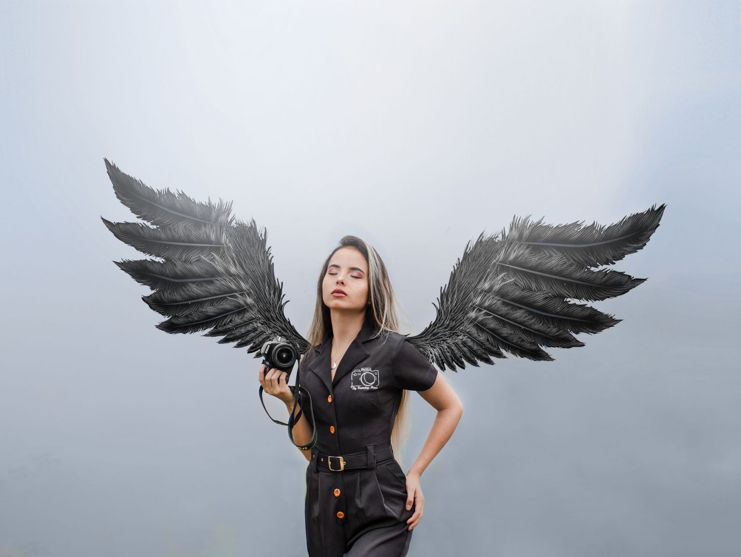 Figure in black outfit poses with dramatic black wings against misty background.