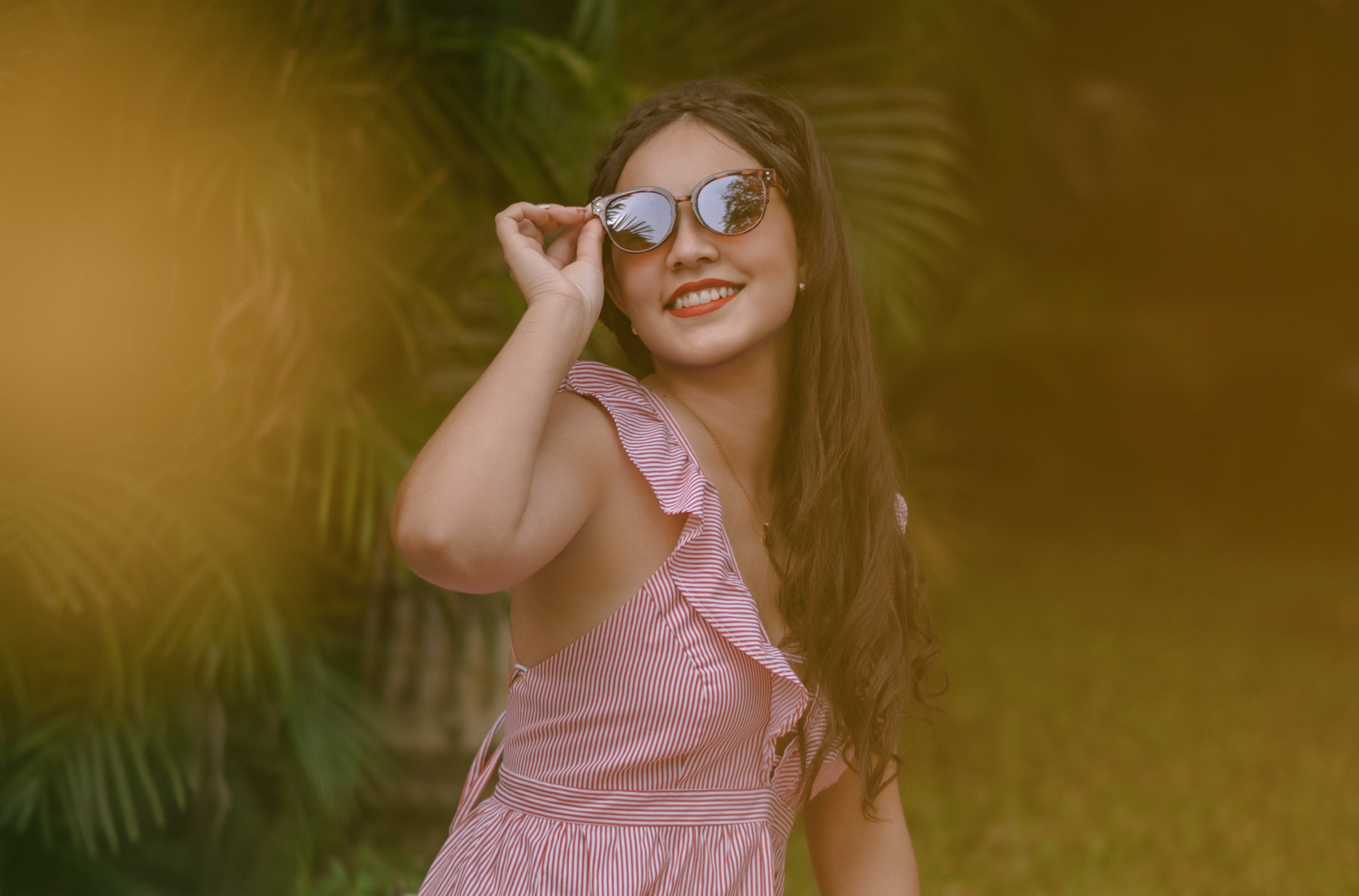 A summery portrait with warm golden lighting and palm fronds in the background.
