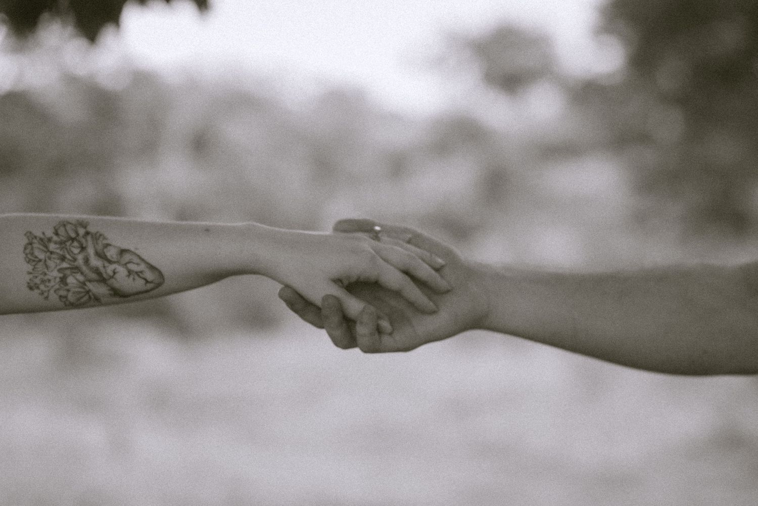 Black and white photo of two hands reaching towards each other with a decorative tattoo visible.