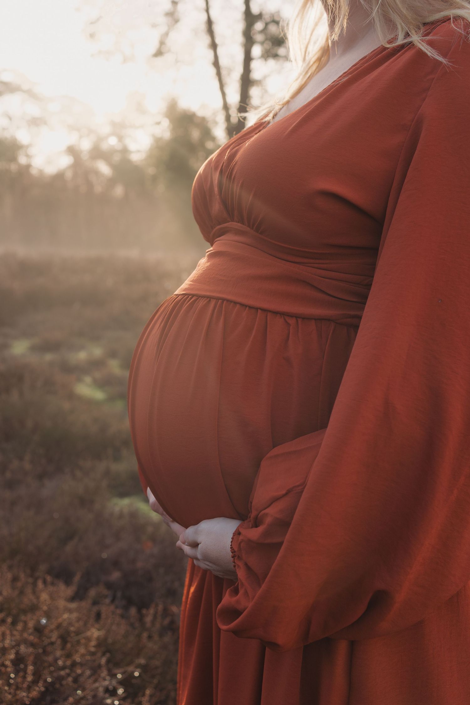 Close-up van een zwangere buik tijdens een zwangerschapsshoot op de heide bij zonsopgang