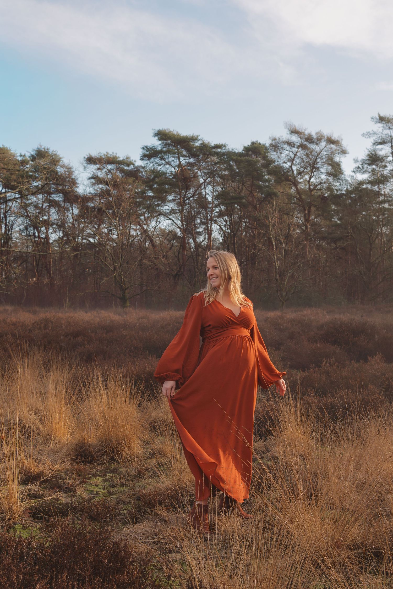 Zwangere vrouw in lange jurk tijdens een zwangerschapsshoot op de heide bij zonsopgang