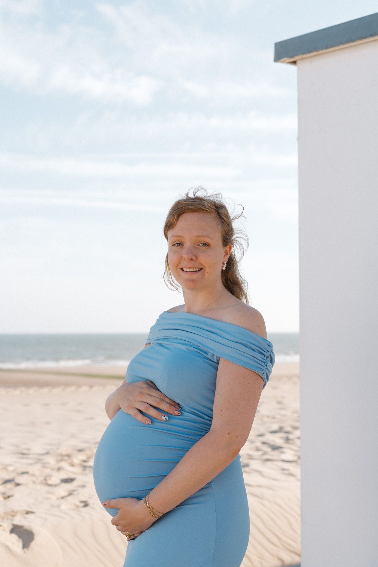 Zwangere vrouw in blauwe jurk tijdens een zwangerschapsshoot op het strand