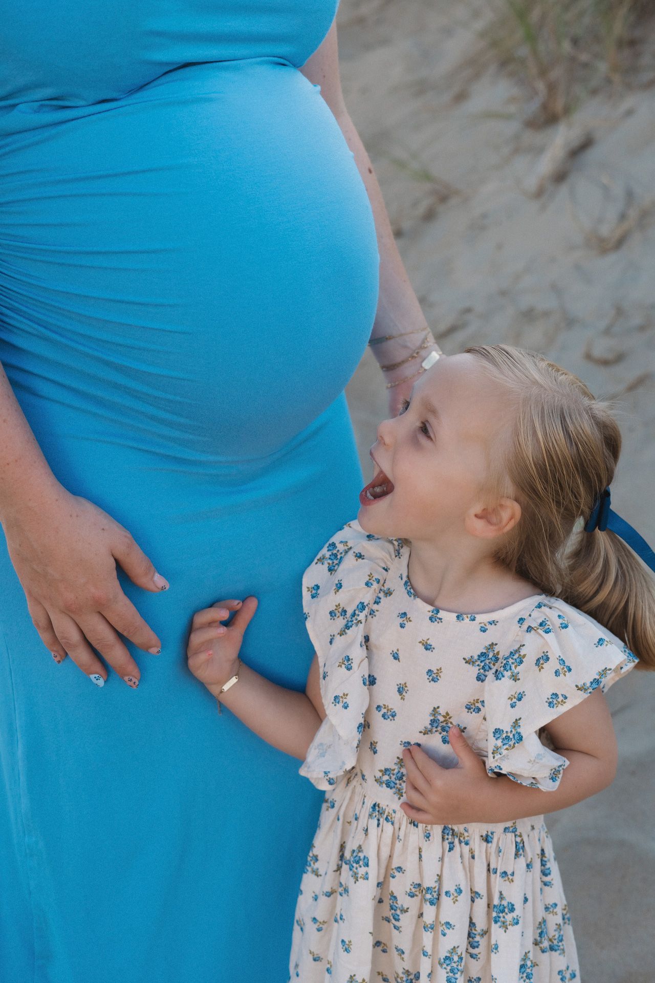 Dochter bij de babybuik van haar mama tijdens een zwangerschapsshoot op het strand