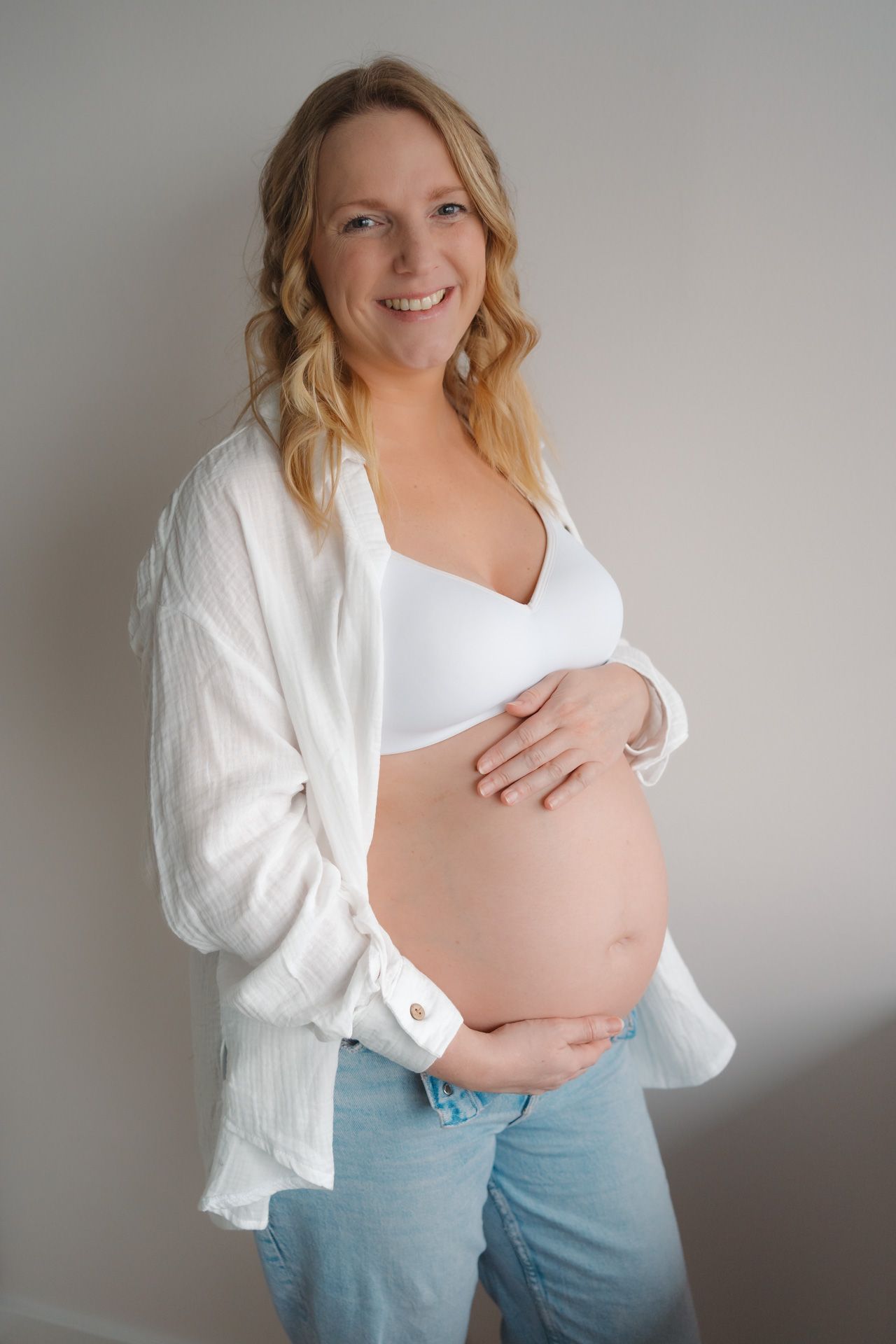 Zwangere vrouw met handen op de babybuik tijdens een zwangerschapsshoot bij haar thuis