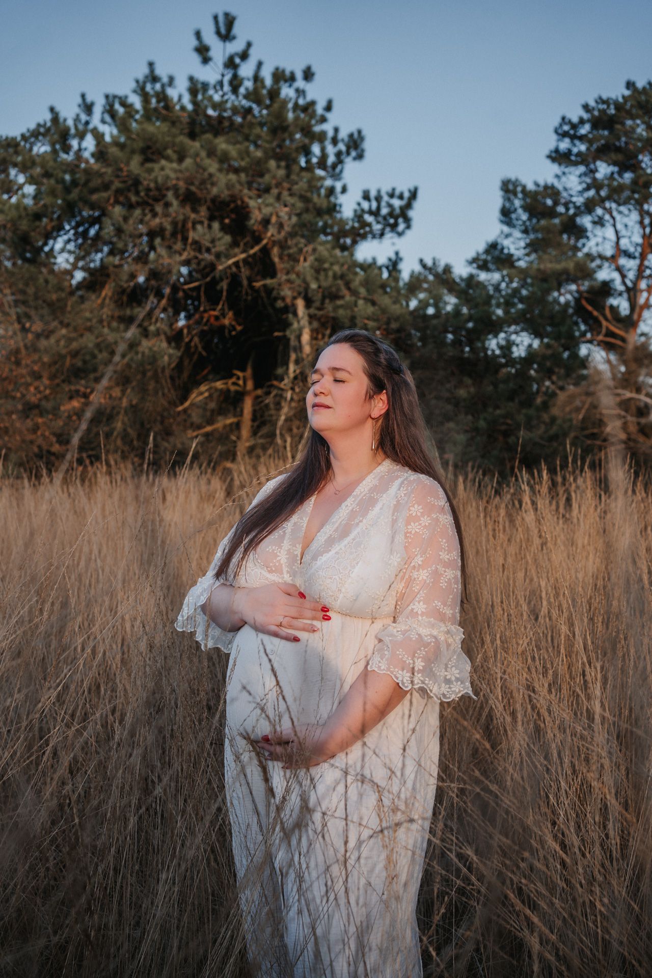 Zwangere vrouw tijdens een zwangerschapsshoot in de natuur bij zonsondergang
