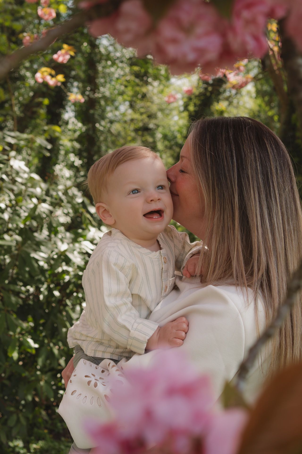Mama geeft haar lachende baby een kus tijdens een gezinsshoot in een park in Mechelen