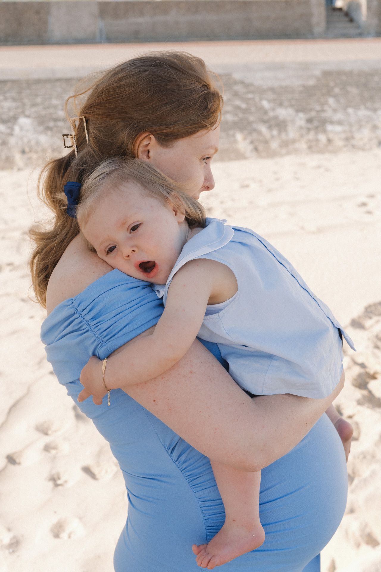 Zwangere mama knuffelt haar dochter tijdens een zwangerschapsshoot op het strand