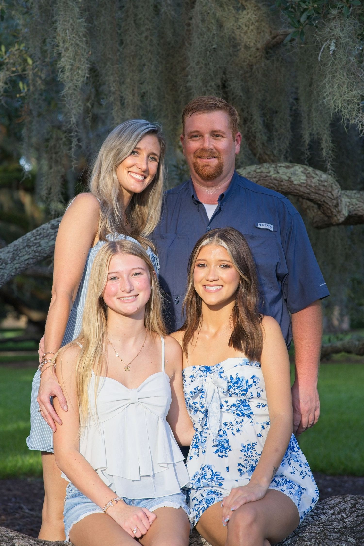 Family of four posing under a large oak tree with Spanish moss in a lush green park.