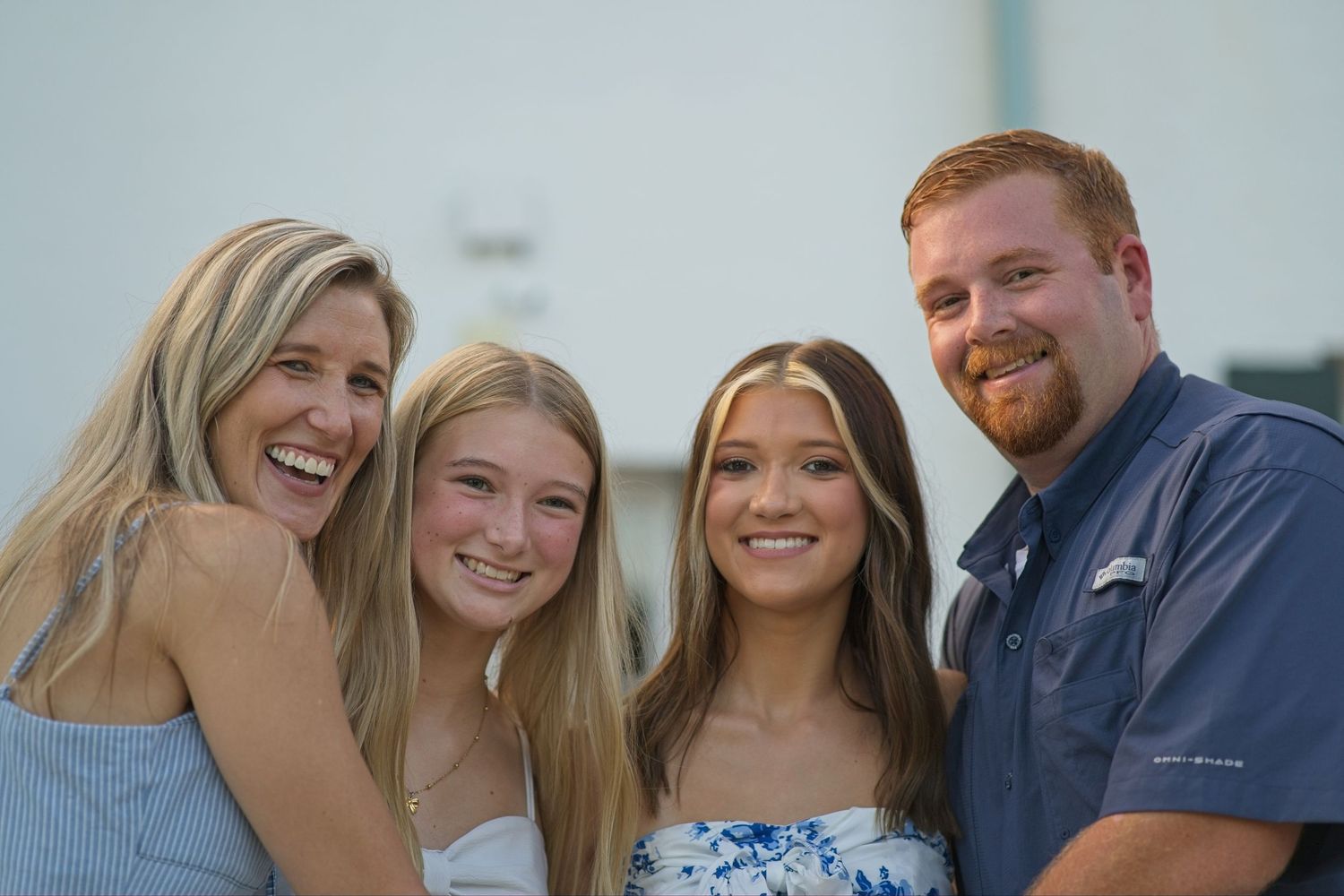 Happy family of four laughing together outdoors during a warm summer evening photo session.