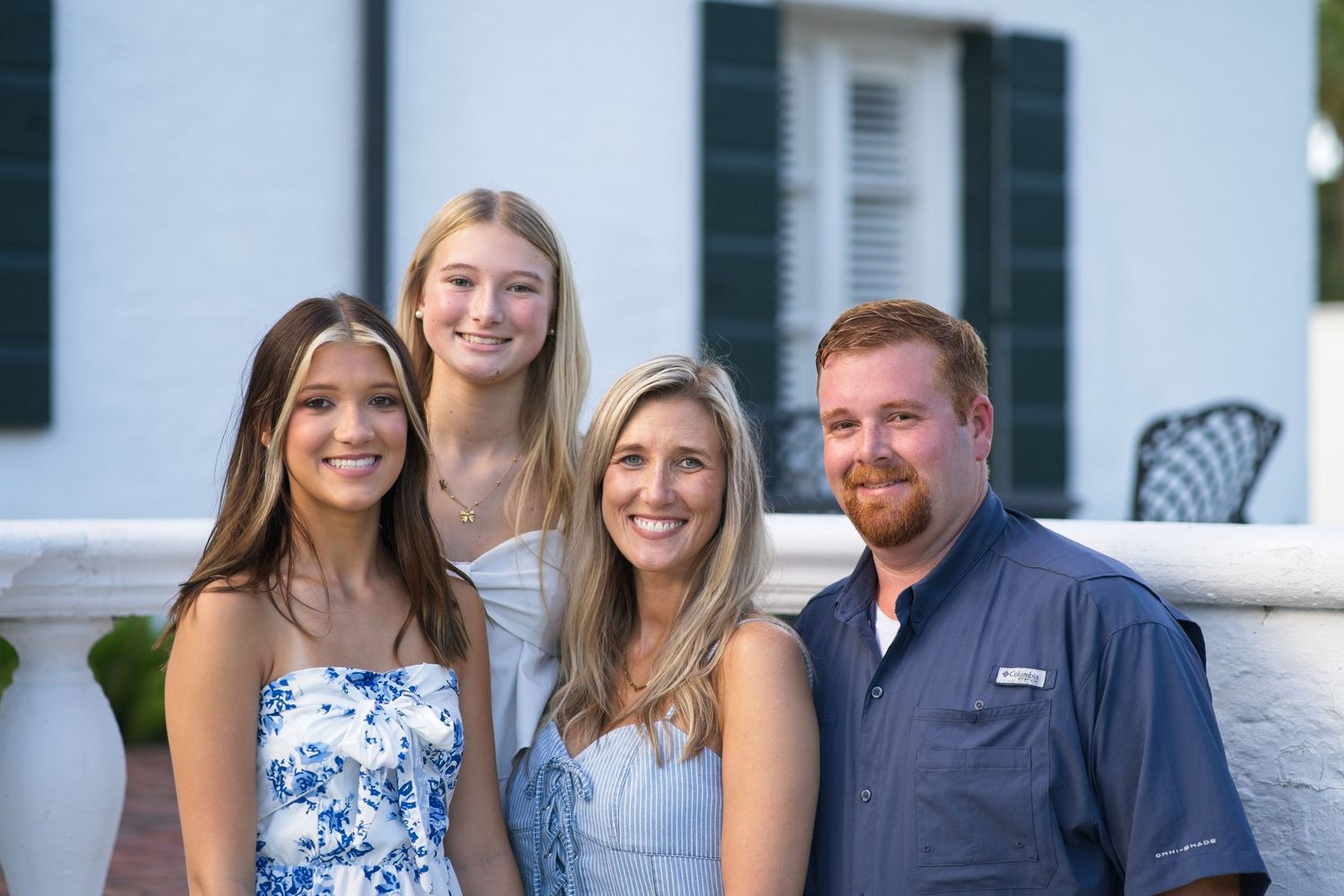 Family of four smiling together outdoors in front of a white building at golden hour.