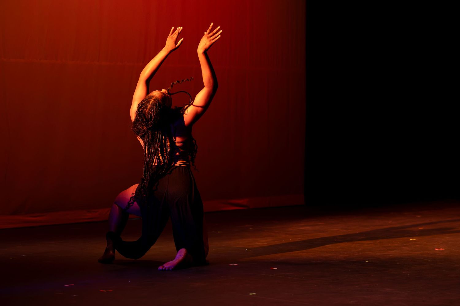 Female dancer performs an expressive kneeling solo under dramatic red stage lighting.