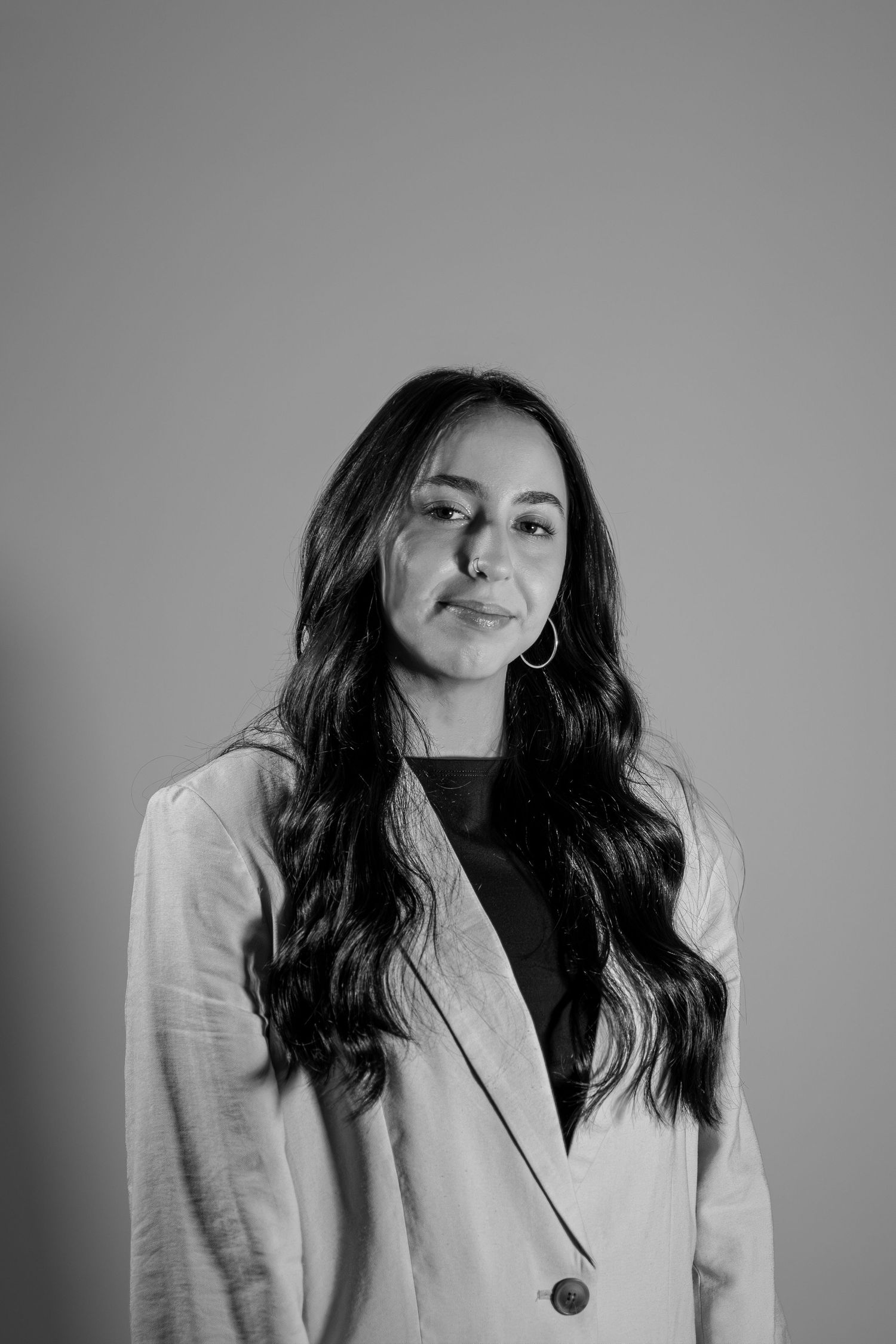 Black and white portrait of a woman with long wavy hair wearing a blazer and hoop earrings.