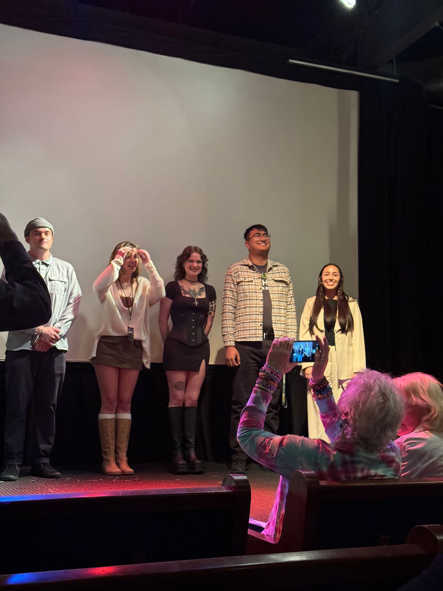 Five performers taking a bow on stage after a theater production under bright lights.