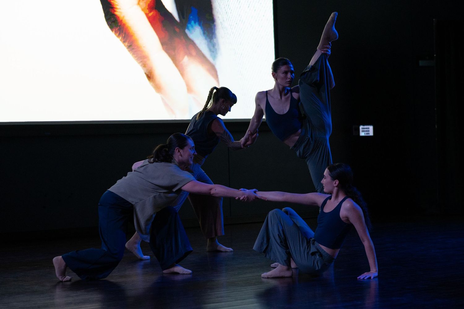 Group of contemporary dancers perform together with a projected screen backdrop on stage.