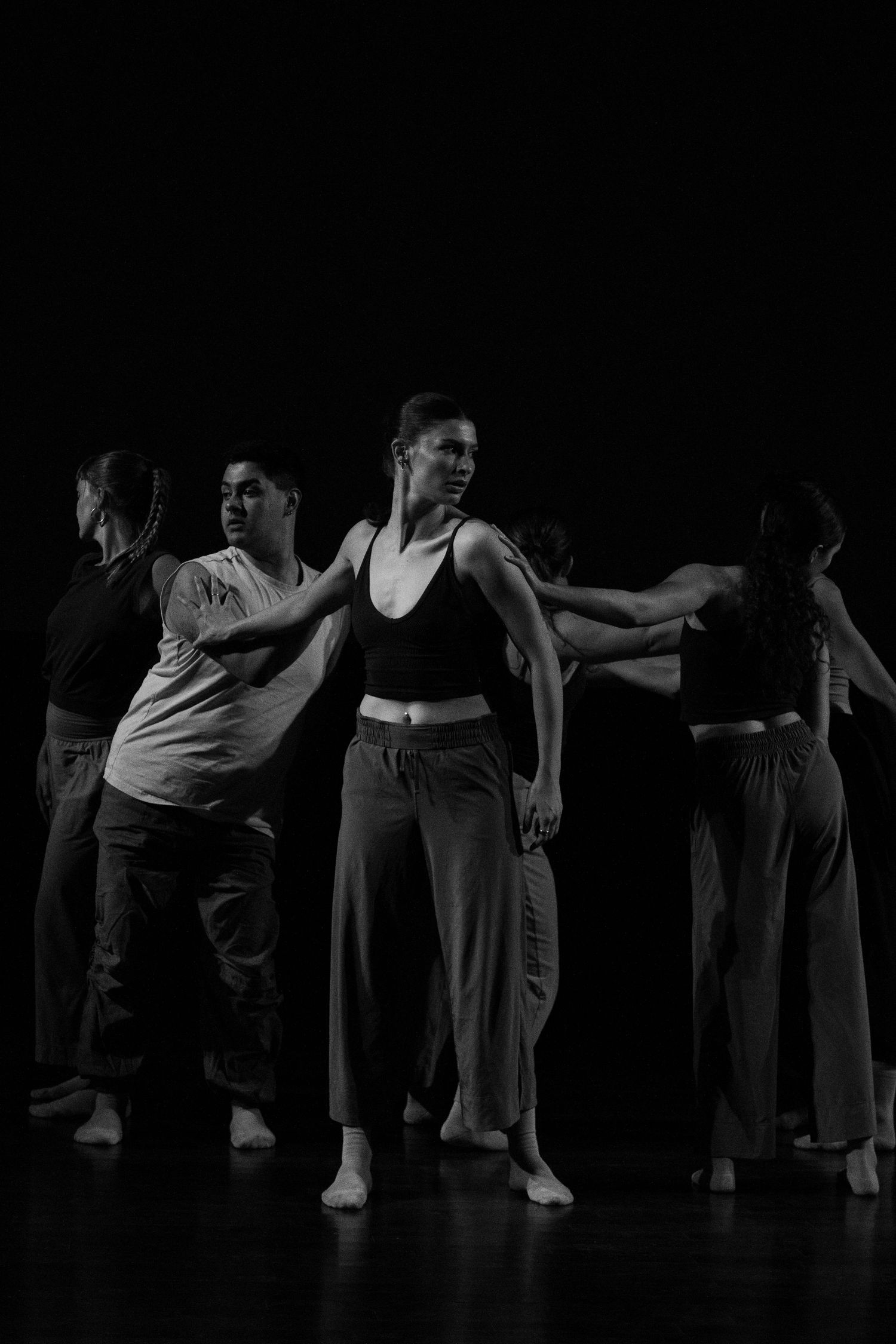 Black and white photo of five contemporary dancers performing on a dark stage.