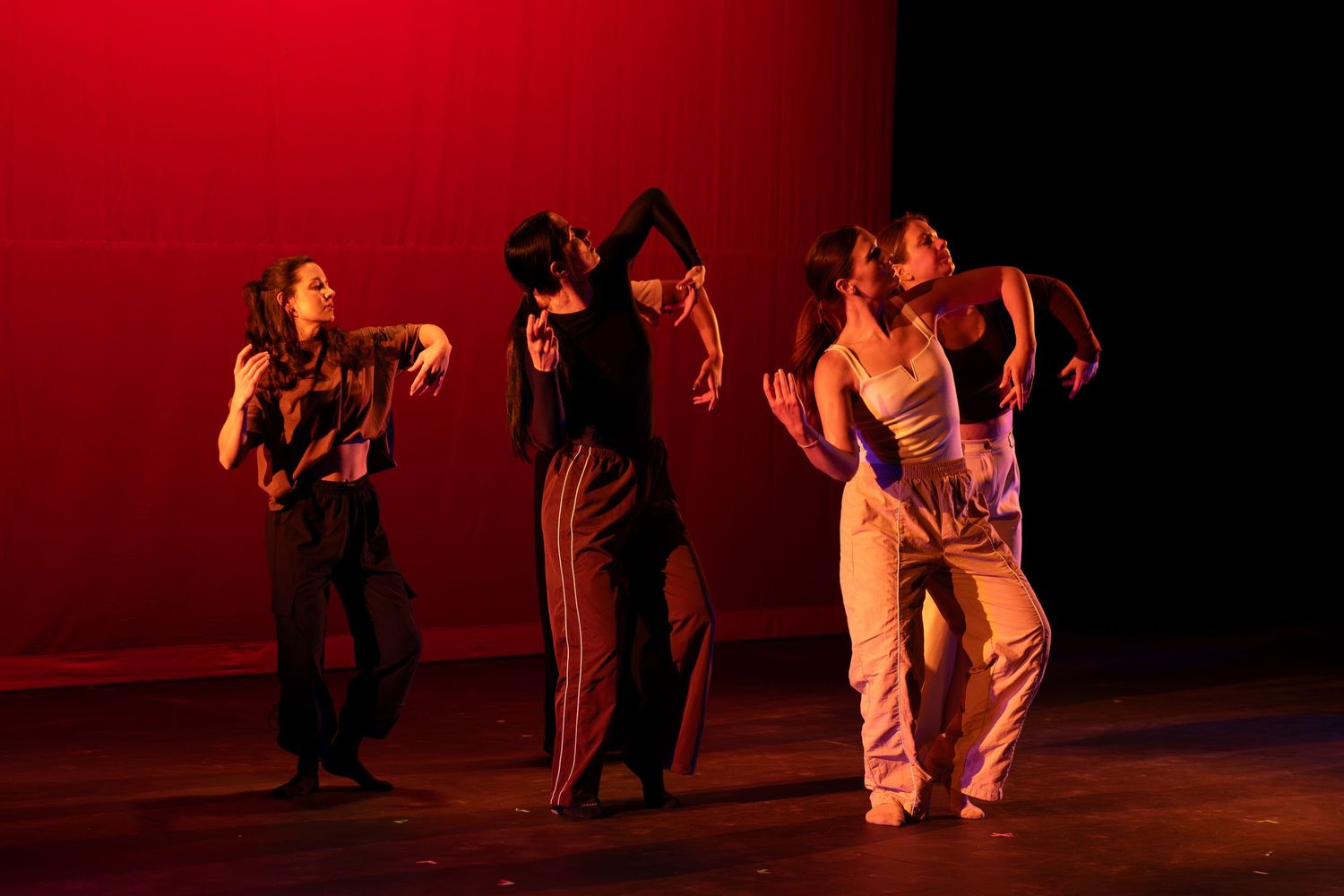 Four contemporary dancers perform expressive choreography under warm red stage lighting.