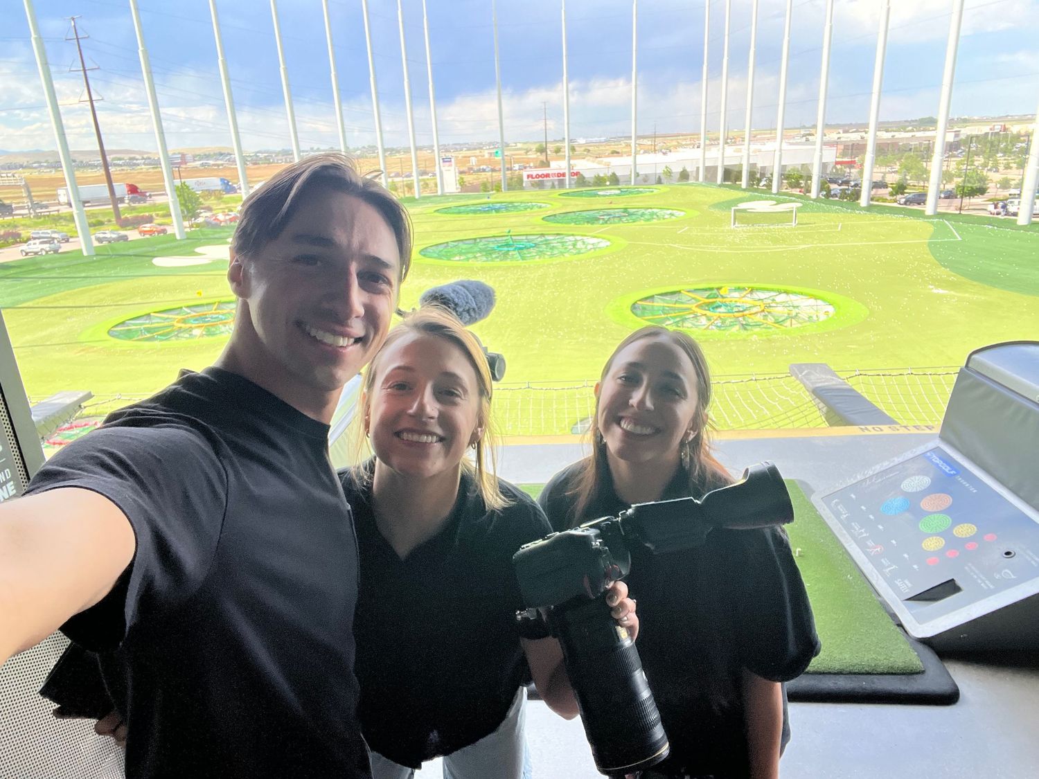 Three media production crew members taking a selfie at a Topgolf venue with cameras.