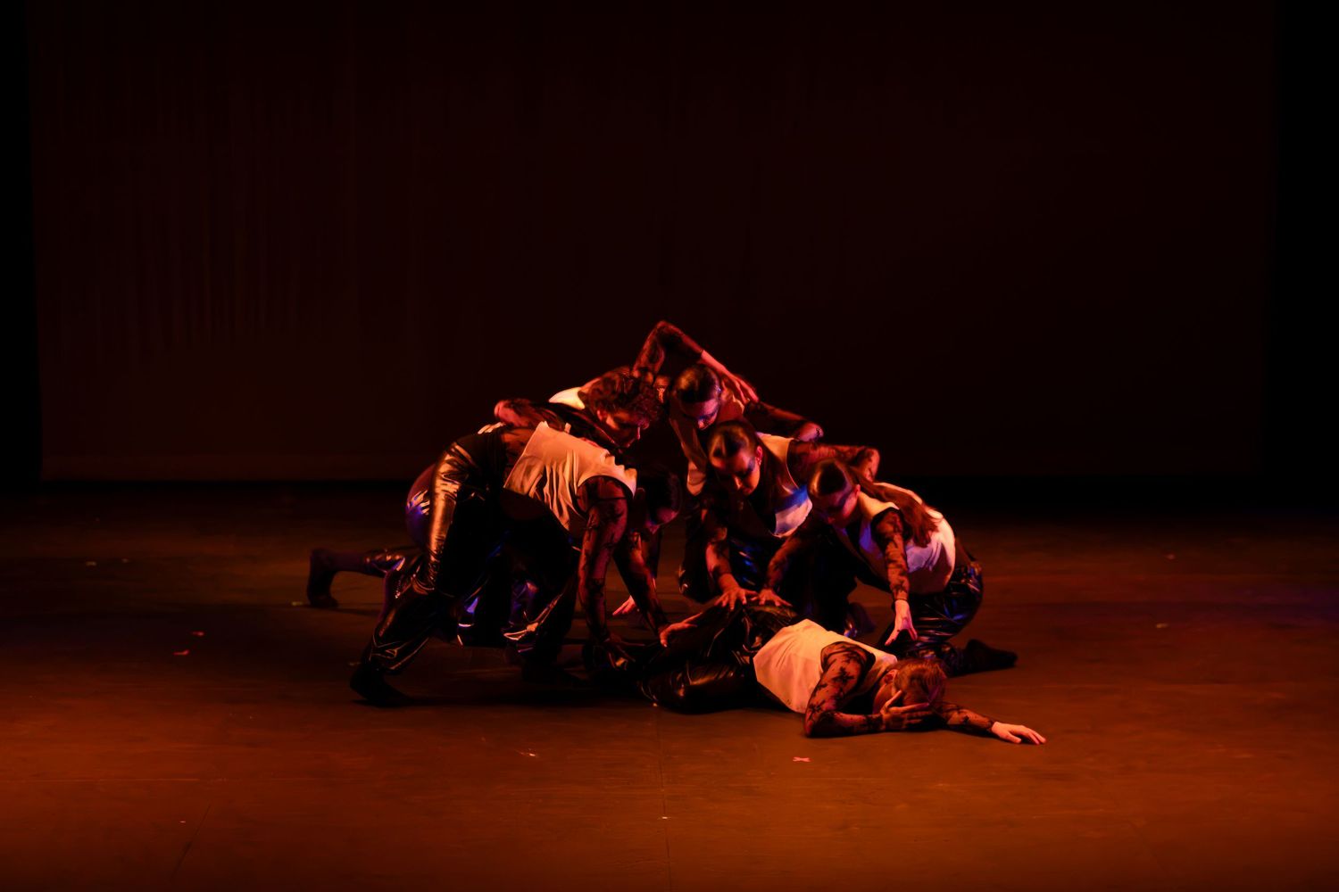 A group of dancers form a dramatic pile on a warmly lit stage during a performance.