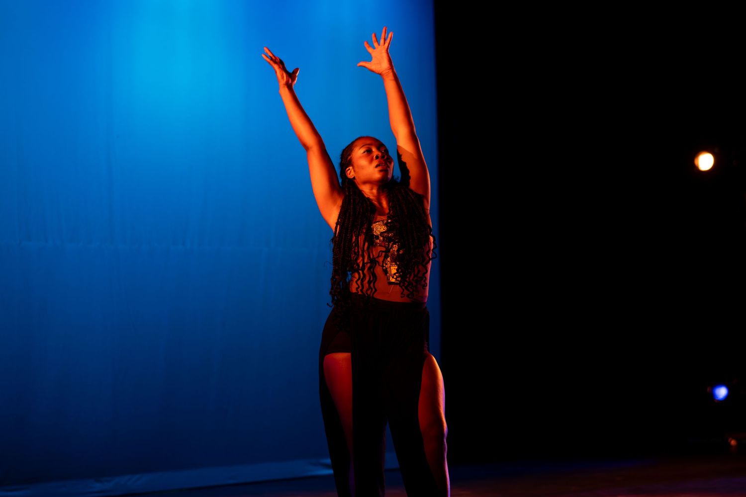 Female dancer reaches arms overhead under vibrant blue stage lighting during a solo performance.