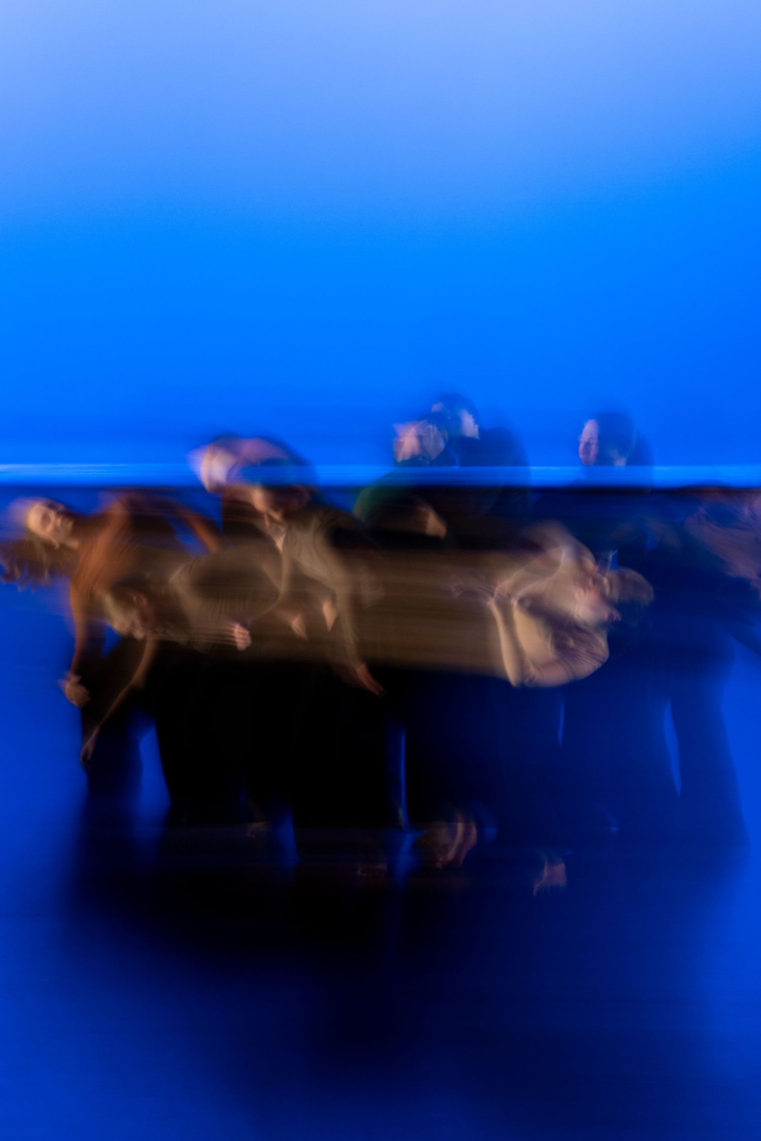A group of dancers captured in motion blur under vivid blue stage lighting in a contemporary performance.