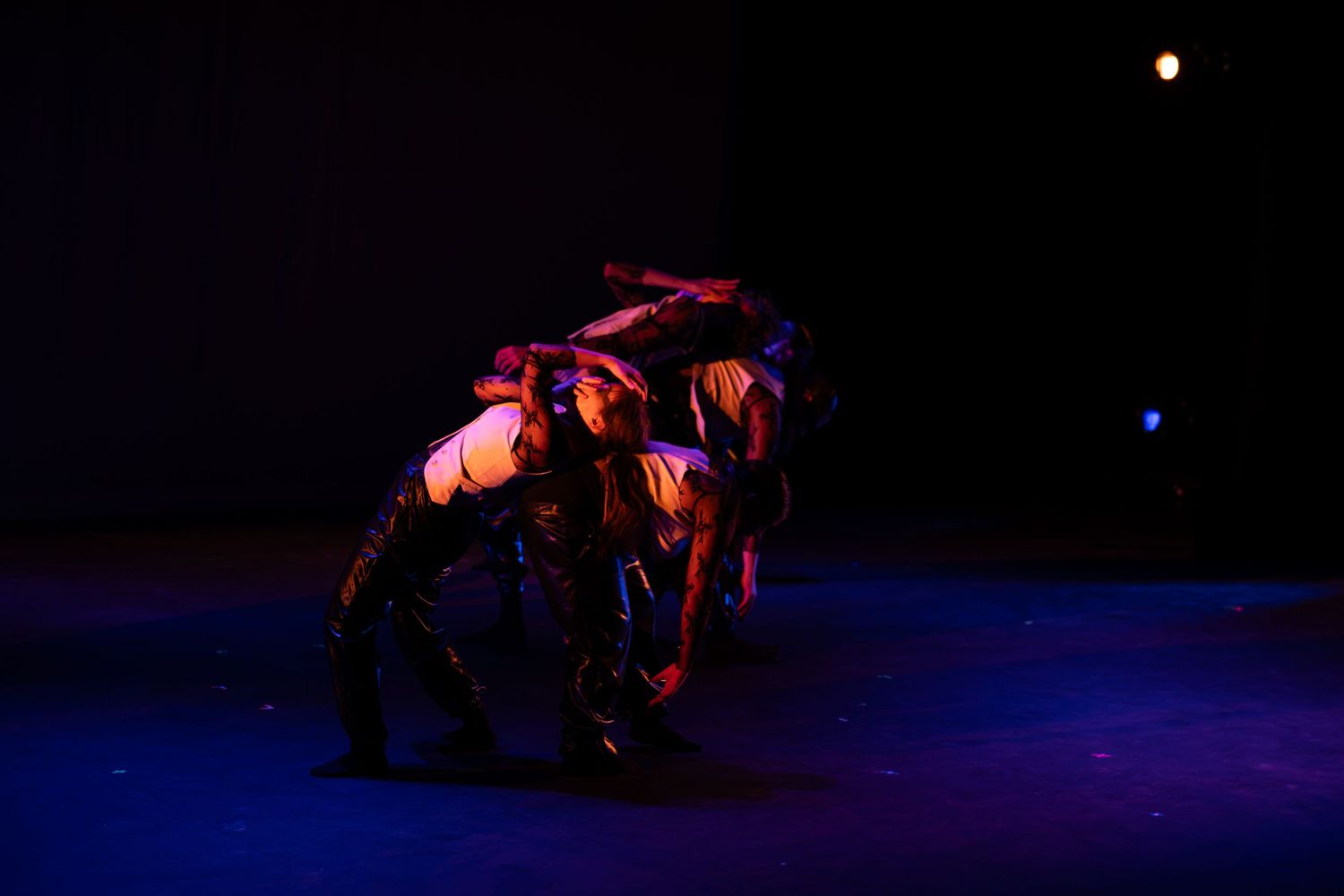Contemporary dancers performing an acrobatic floor routine under moody blue and red stage lighting.