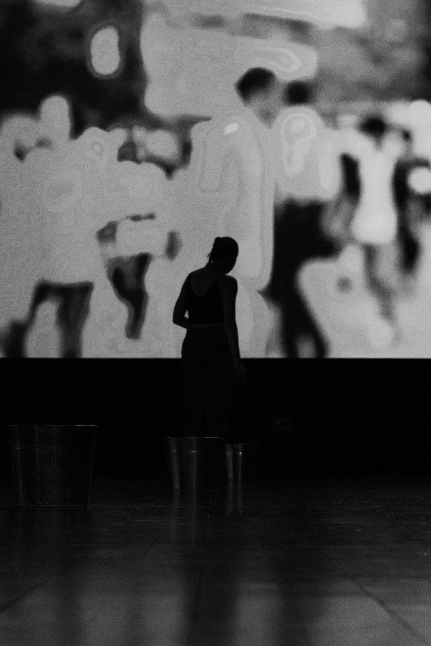 Silhouetted dancer stands before a large abstract projected image on stage.