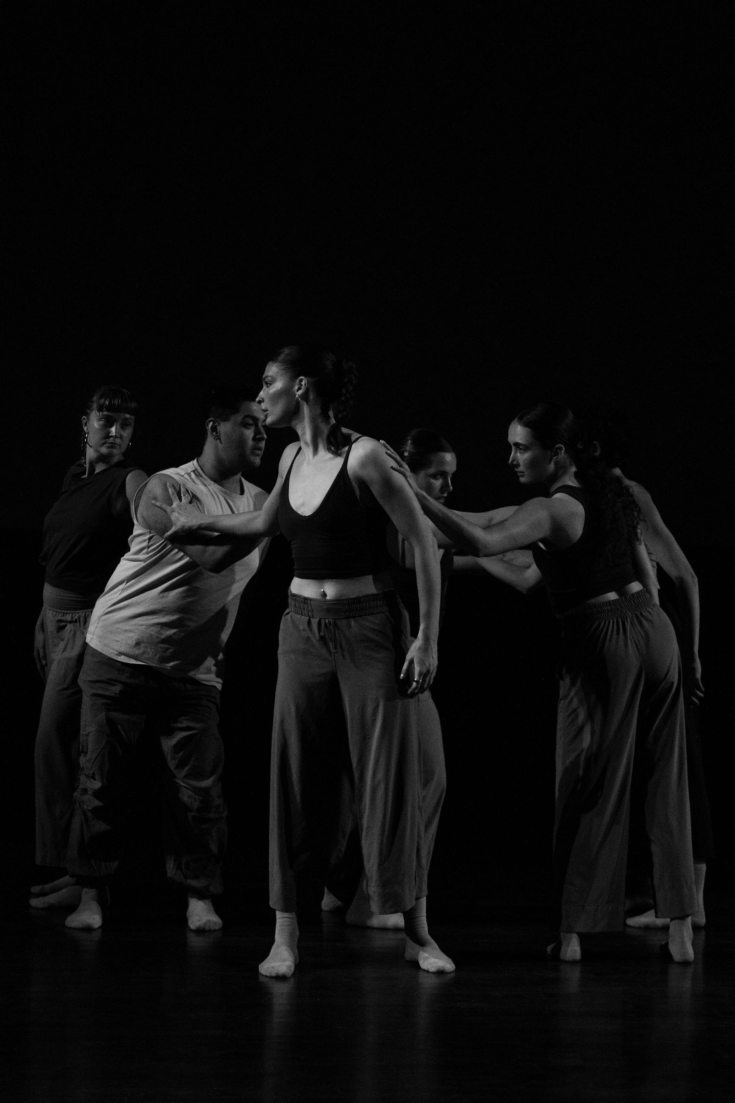 Five contemporary dancers perform an ensemble piece on a dimly lit dark stage.