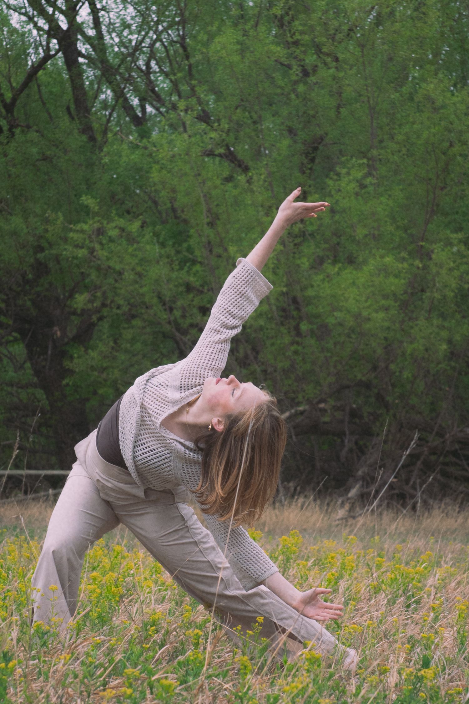 A woman performs a graceful triangle yoga pose in a wildflower meadow surrounded by lush green trees.