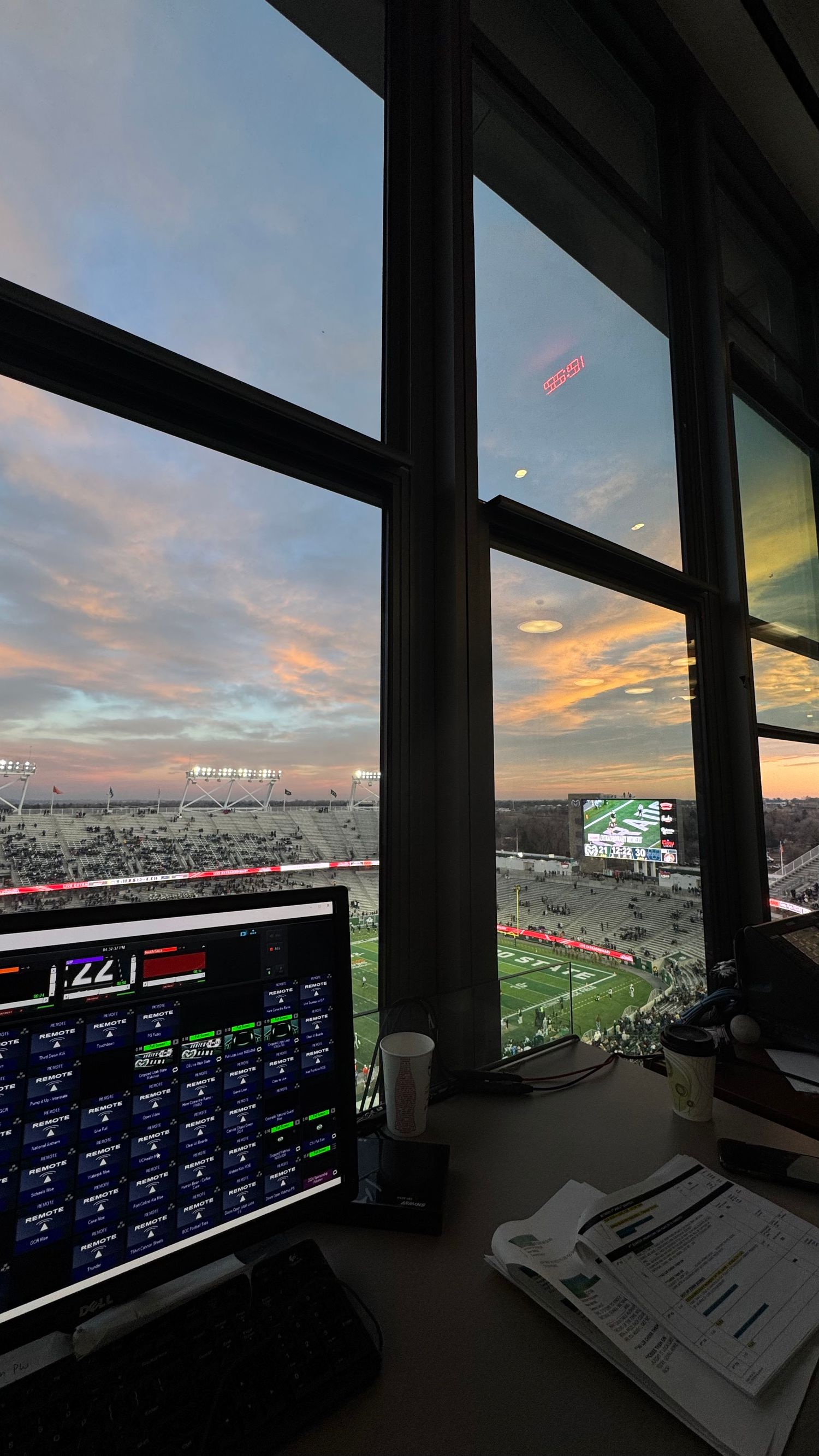 Football stadium press box view at sunset with broadcast monitoring equipment in foreground.