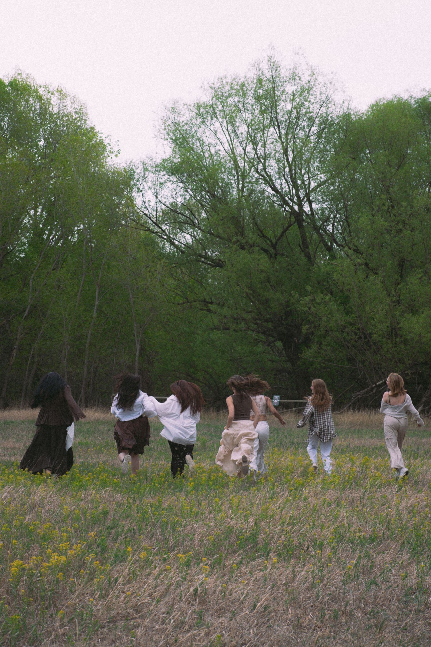 Group of women running through a wildflower meadow with lush green trees in the background.