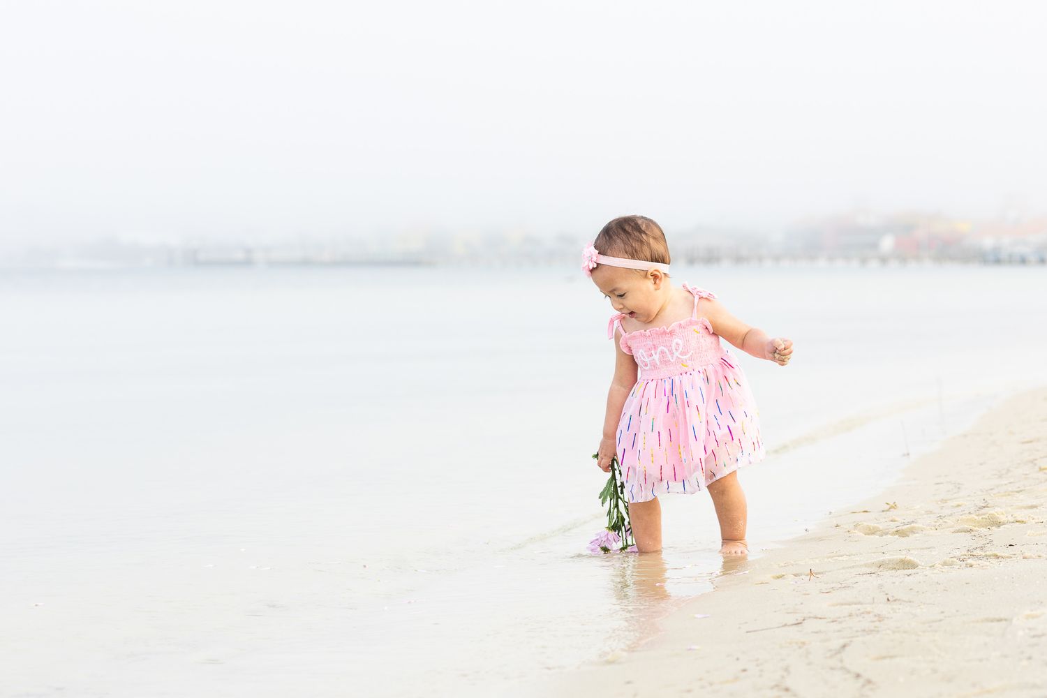 Baby girl in a pink dress toddling along the shoreline