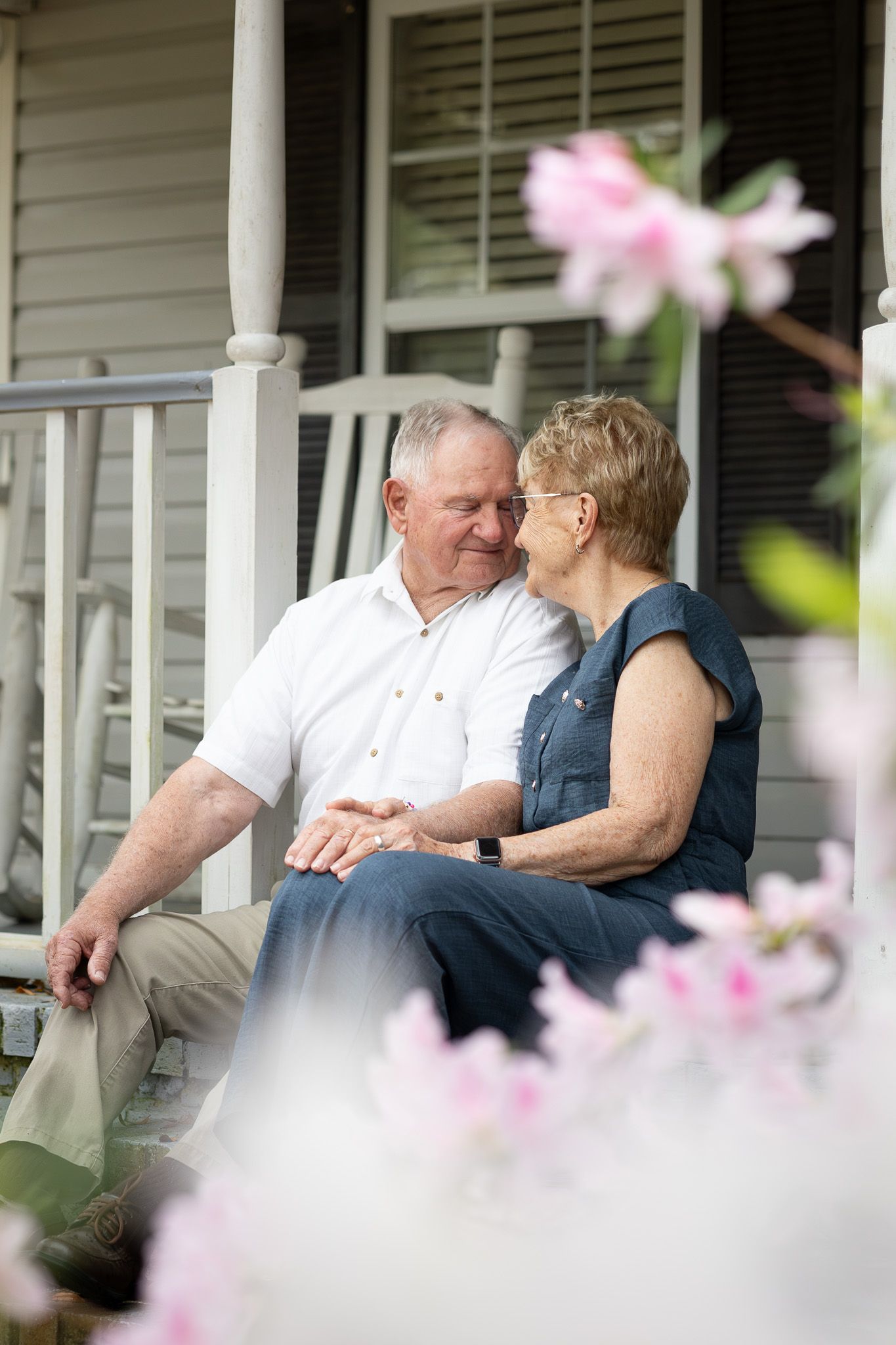 Grandparents sitting together on their front porch surrounded by pink azaleas