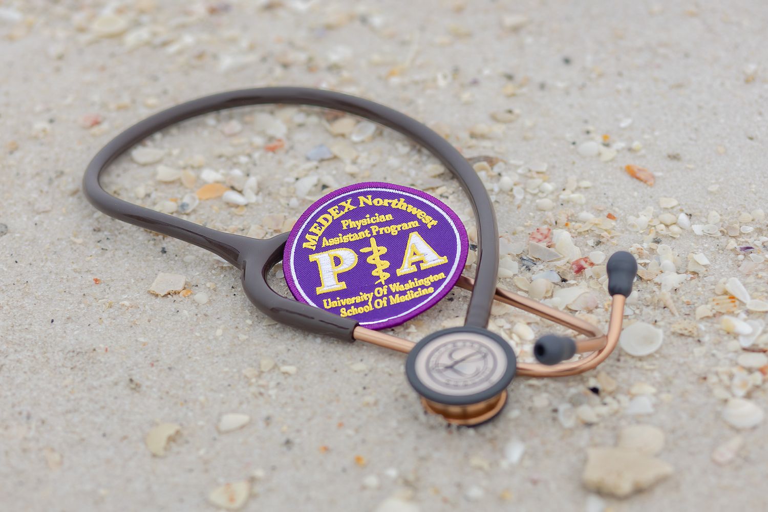 Stethoscope and white coat patch resting in the sand