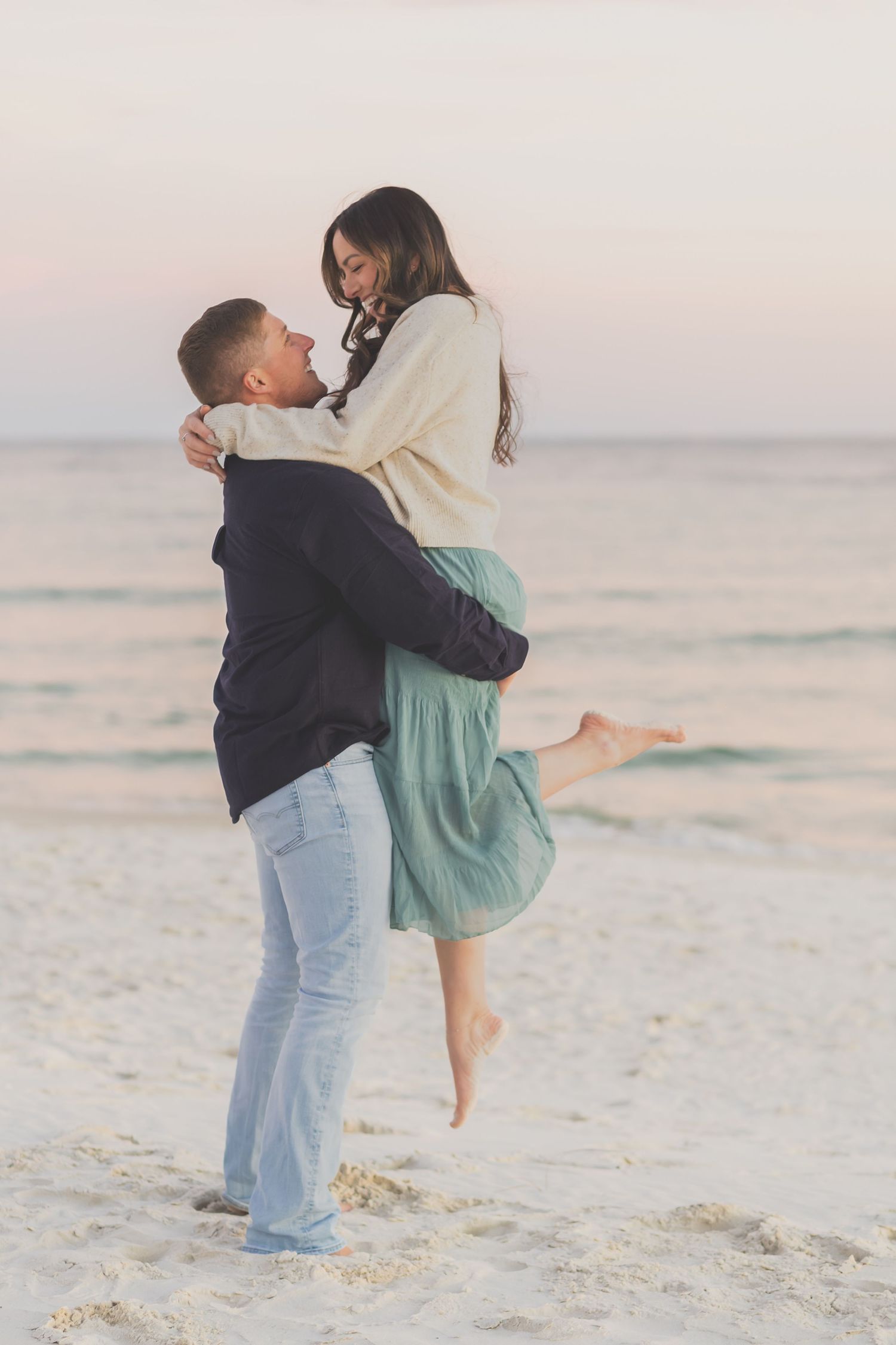 Man lifting his partner in a hug on the beach at sunset