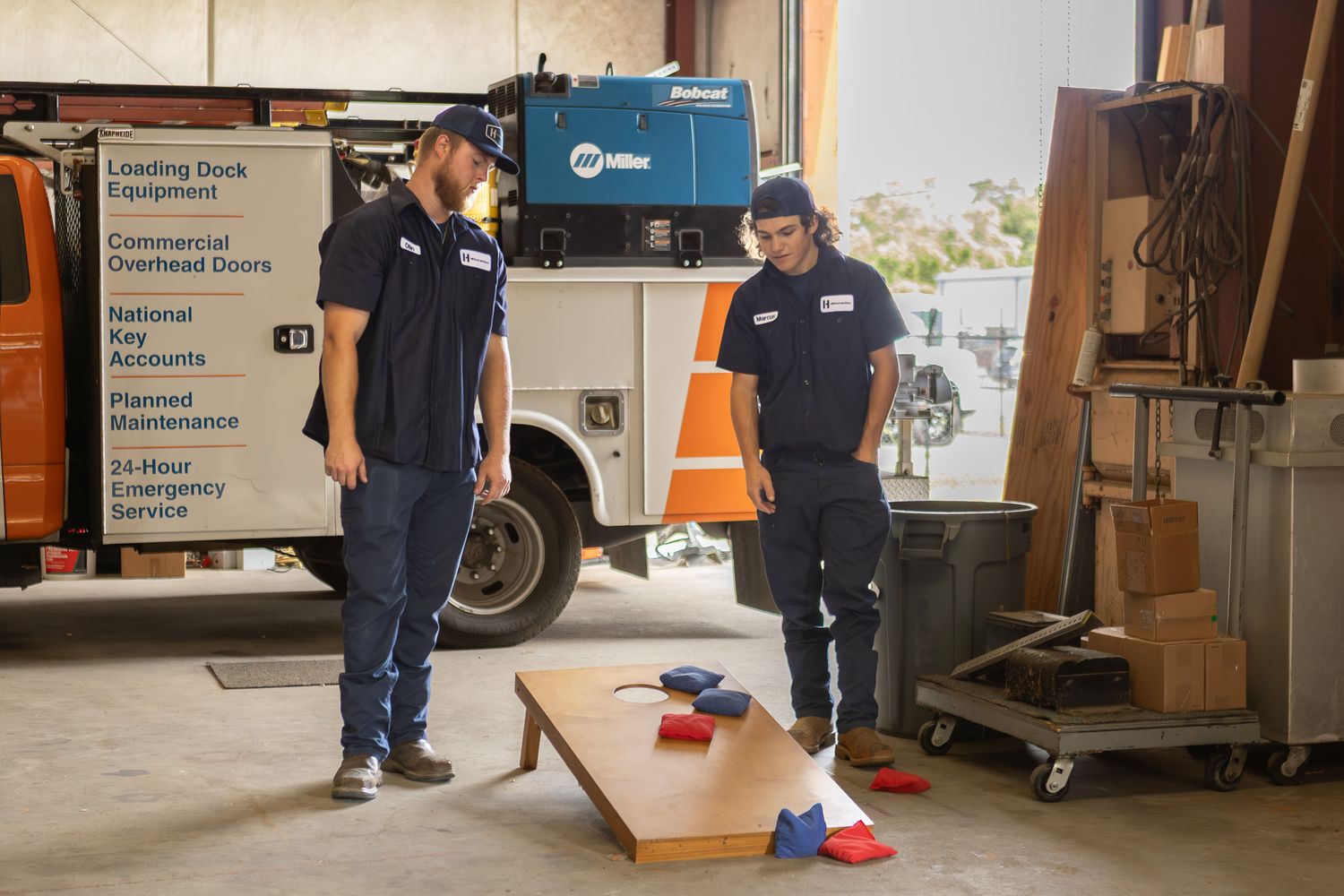 Coworkers playing cornhole next to a work truck at a company event