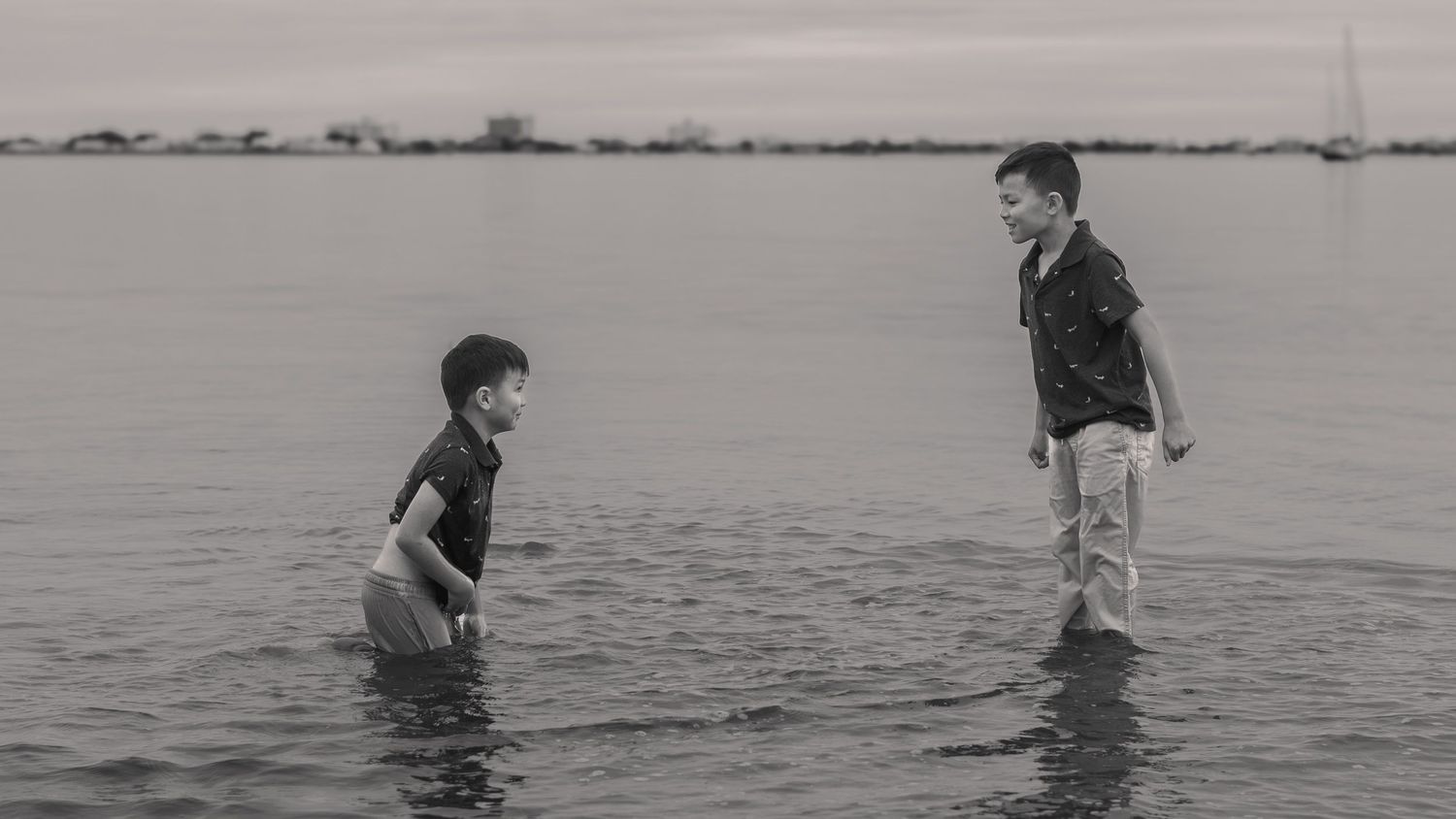 Two children wading in calm bay water at sunset