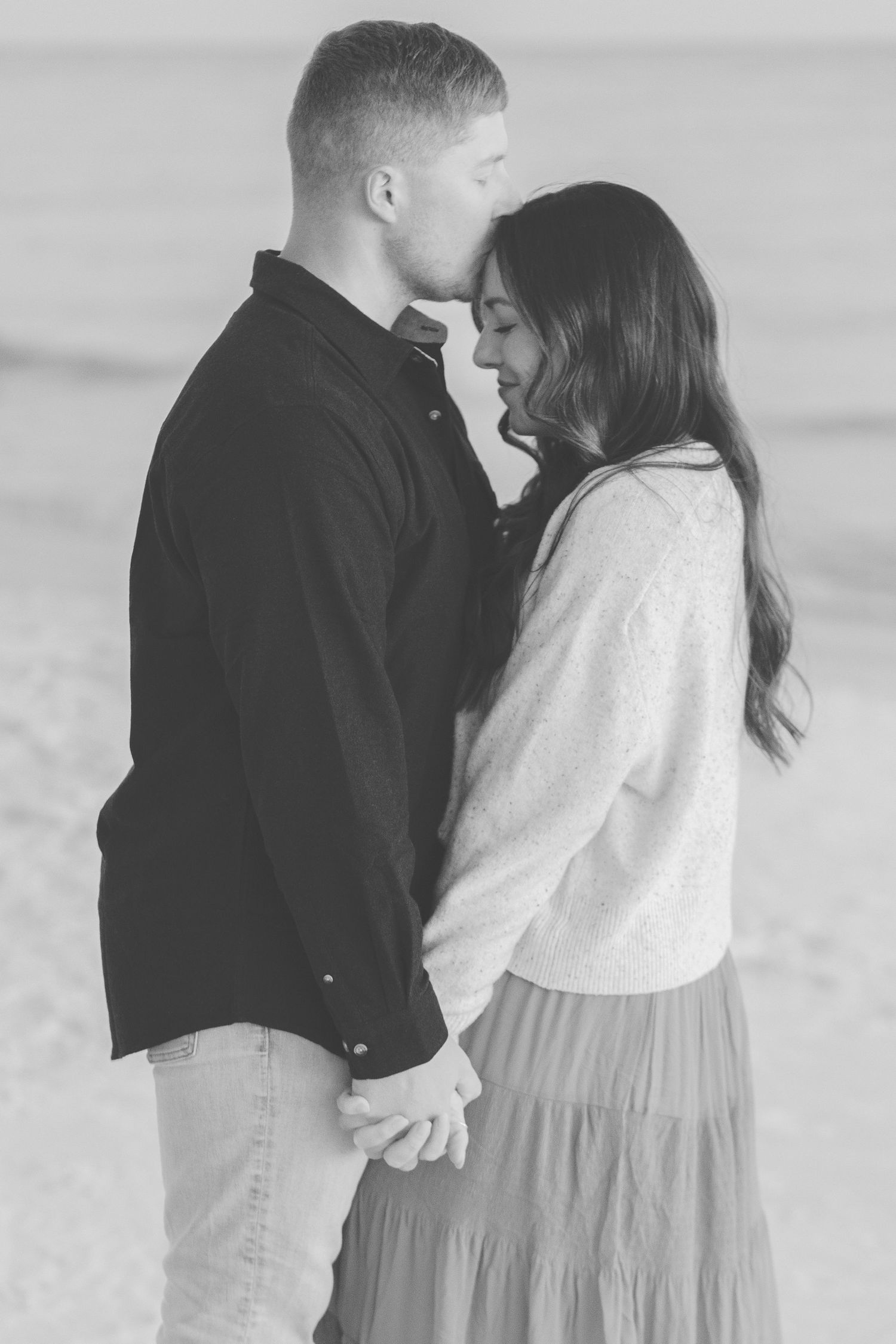 Black and white photo of a man kissing his partner's forehead on the beach