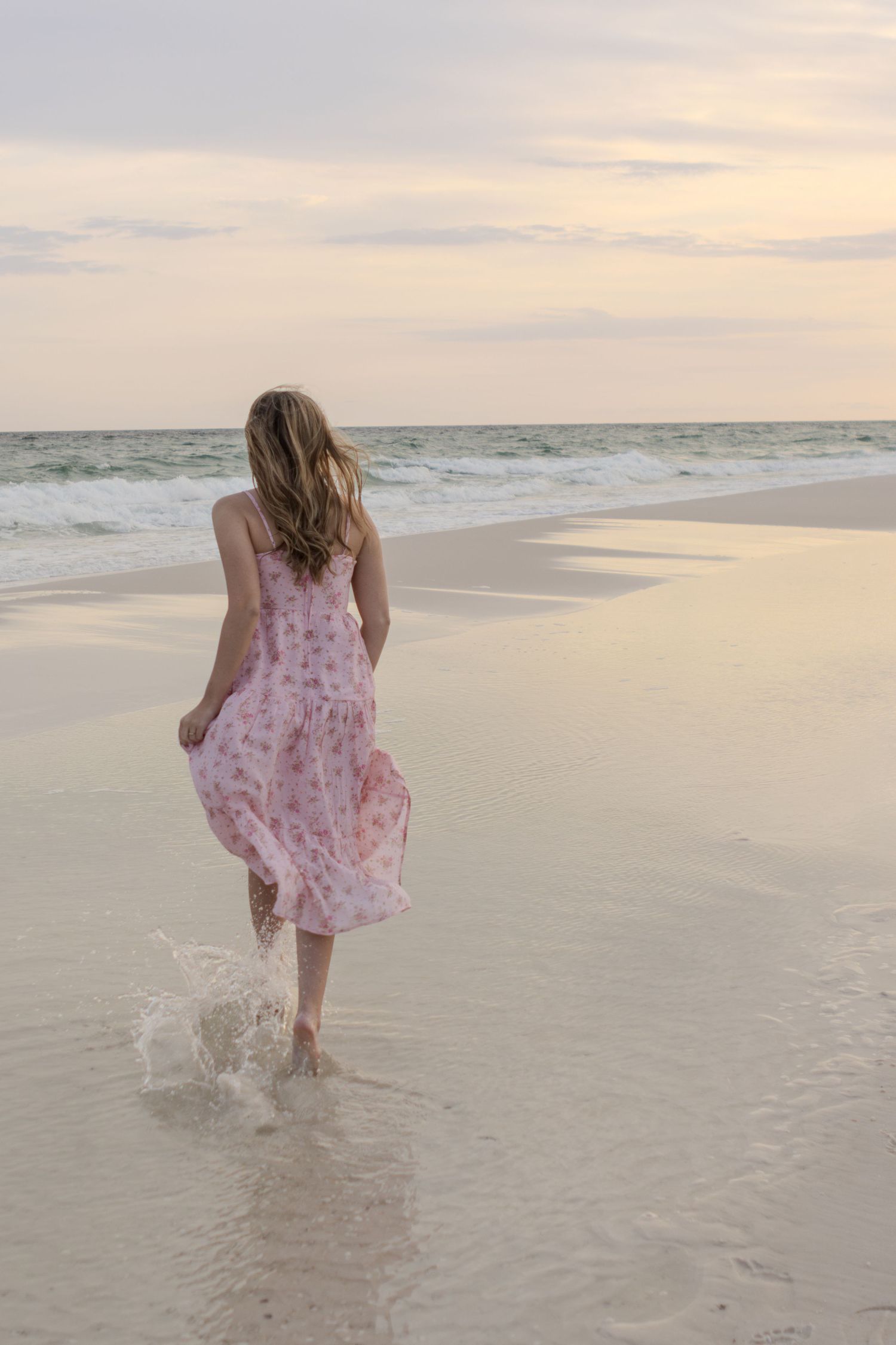 Young woman walking through the shallow water at sunset