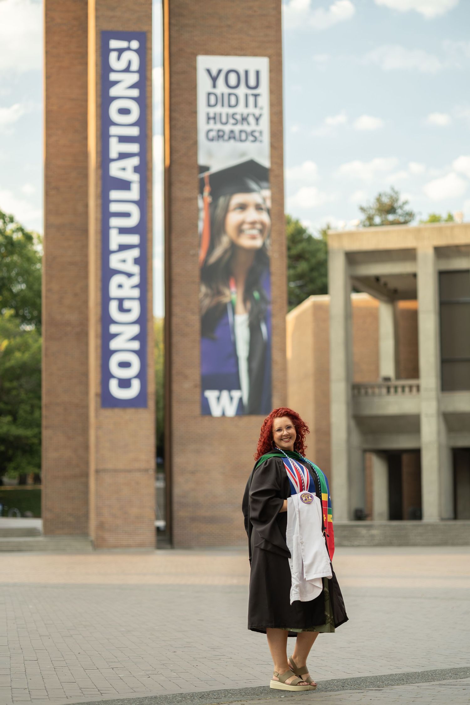 College graduate in cap and gown beside a Congratulations banner on campus