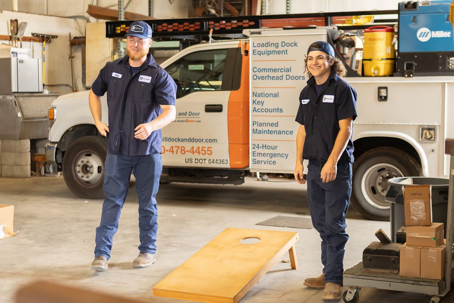 Two employees playing cornhole in a company warehouse at a work event