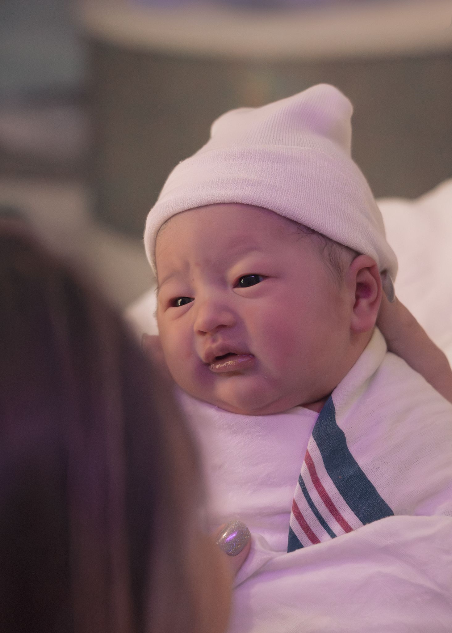 Newborn baby in a striped hospital blanket and knit hat