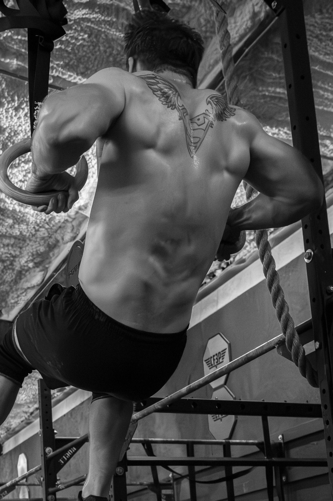 Black and white photo of a muscular athlete climbing a rope at the gym