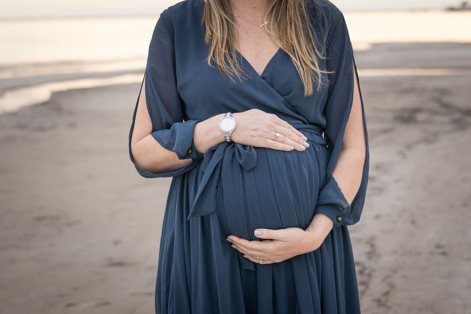 Expecting mother in a navy dress cradling her baby bump on the beach