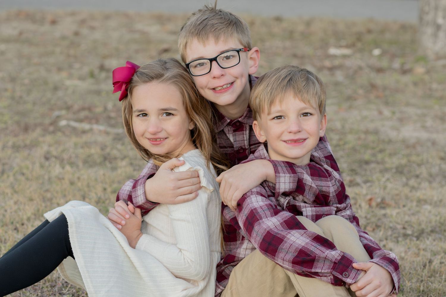 Three siblings sitting together in the grass for fall family photos