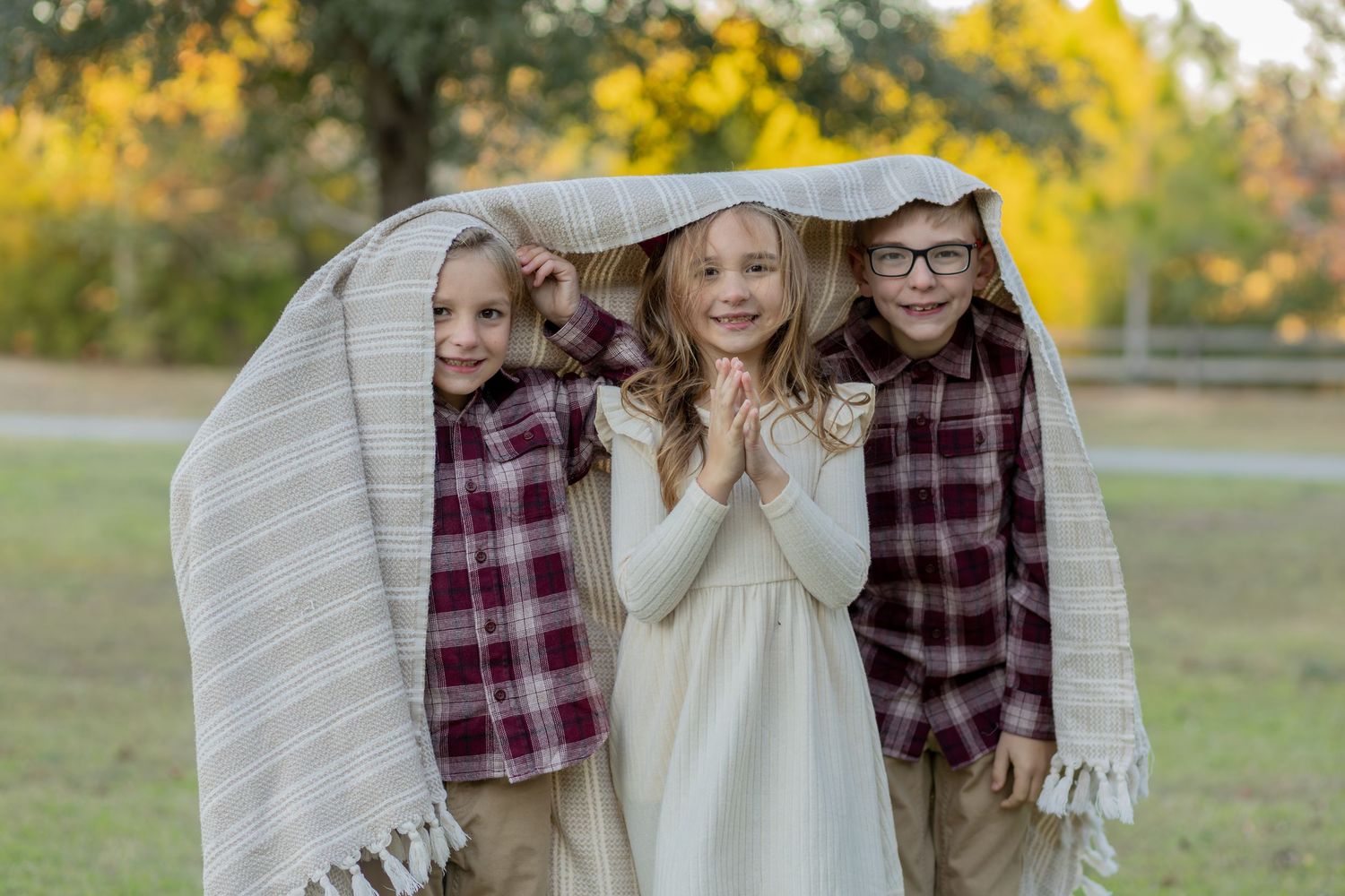 Siblings snuggled under a blanket in a park for fall family photos