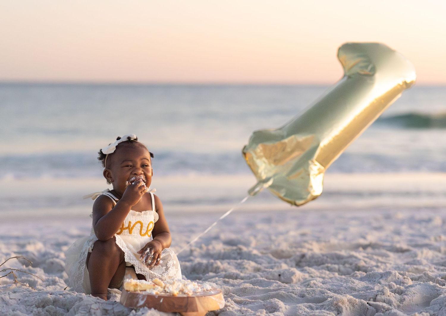 Baby at the beach at sunset with a gold number one balloon