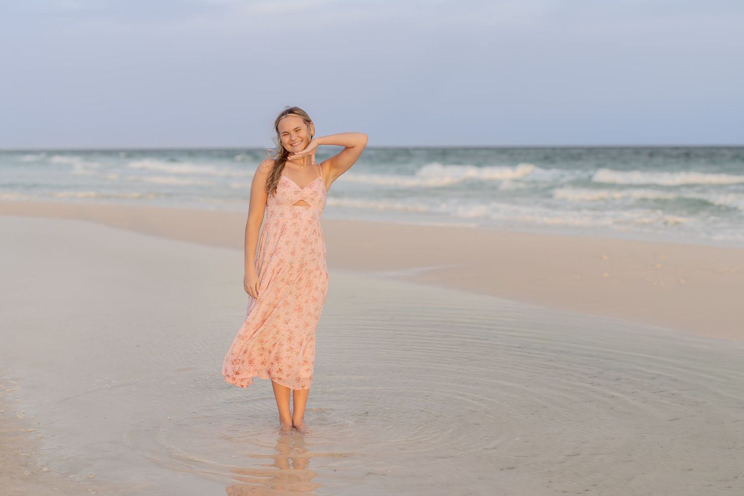 Young woman in a pink dress standing on the beach at sunset